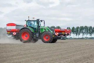 Zelený traktor se dvěma rozmetadly Kverneland na poli.