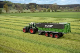 Traktor táhne zelený senážní vůz Fendt Tigo po louce.