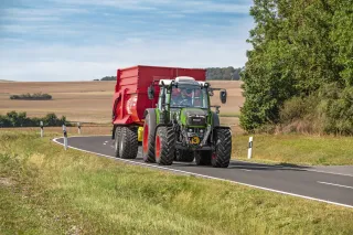 Traktor Fendt 200 Vario táhne červený návěs po silnici.