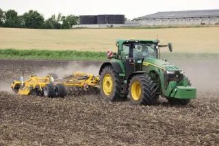 Traktor John Deere 8R 410 se žlutým kultivátorem při práci na poli.