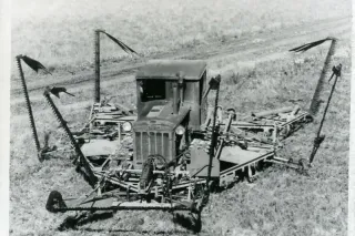 Historický černobílý snímek pásového traktoru s velkoplošným žacím strojem.