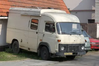 Starší světlý skříňový automobil AVIA zaparkovaný u domu.