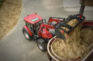 Červený traktor Case IH s čelním nakladačem při práci ve stáji.