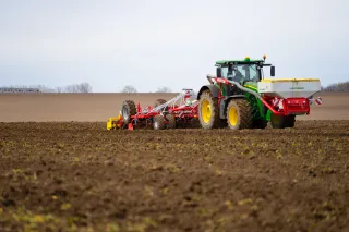 Traktor s radličkovým podmítačem Pöttinger a čelním zásobníkem na poli.