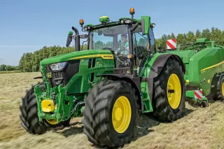 Zelený traktor John Deere s lisem na poli.