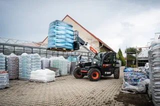 Černý teleskopický manipulátor Bobcat zvedá paletu s vaky.