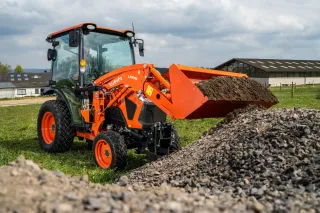 Oranžový traktor Kubota s nakládací lopatou nabírá zeminu.