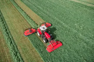 Traktor s červenou žací kombinací Kverneland při sečení louky.