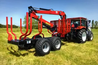 Traktor s červenou vyvážecí soupravou AGAMA na louce.