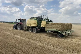 Traktor s lisem Krone Big Pack a vozíkem s balíky slámy na poli.