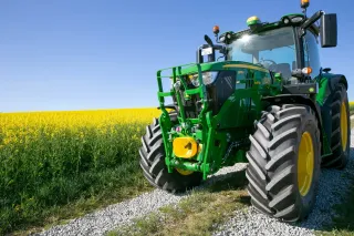 Zelený traktor John Deere u žlutého pole řepky.