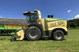 Samojízdná řezačka Krone na louce u odvozního vozu.