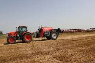 Traktor s taženým postřikovačem Kverneland iXtrack T4 na poli.