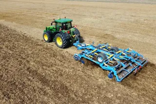 Traktor John Deere s modrým půdním strojem Farmet na poli.