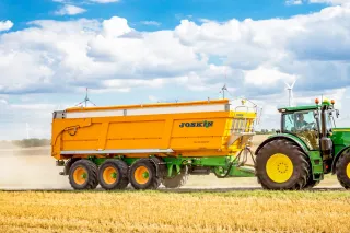 Traktor s oranžovým třínápravovým návěsem Joskin na poli.