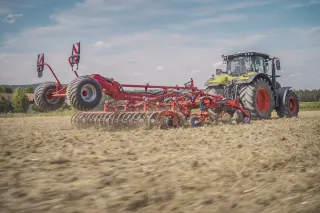 Traktor táhne červený kultivátor Kverneland Enduro T po poli.