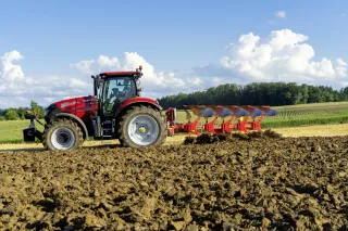 Červený traktor s otočným pluhem Pöttinger SERVO 4000 při orbě.