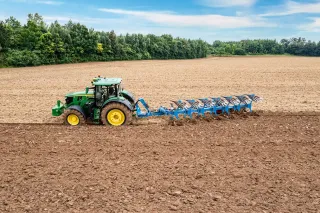 Zelený traktor táhne modrý pluh Lemken Diamant 16 při orbě.