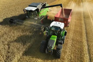 Sklízecí mlátička Fendt sklízí obilí vedle traktoru s přívěsem.