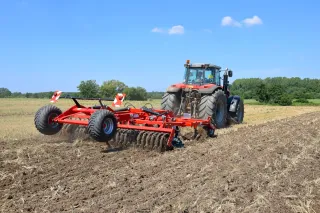 Traktor s červeným diskovým podmítačem SMS CZ ATOS na poli.