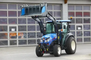 Modrý kompaktní traktor Iseki s čelním nakladačem před halou.