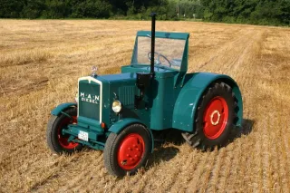 Historický zelený traktor MAN s červenými koly na poli.