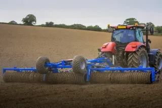 Traktor s modrými válci Dalbo Cambridge na poli.