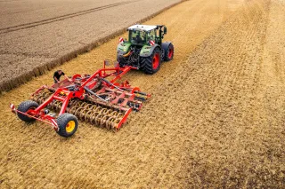 Traktor CLAAS s červeným diskovým podmítačem Väderstad Carrier na poli.