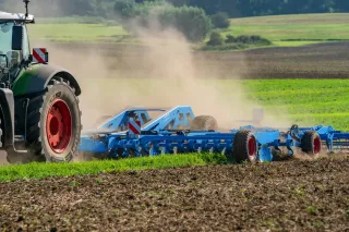 Traktor s modrým kypřičem Lemken Koralin při práci na poli.