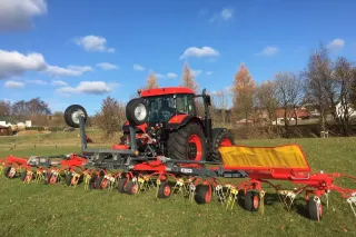Traktor s červeným obracečem pícnin ROZMITAL na louce.