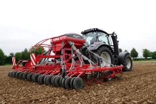 Traktor s červeným secím strojem Kverneland ts-drill na poli.