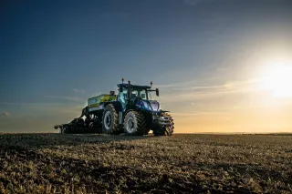Modrý traktor New Holland T7.300 na poli za západu slunce.