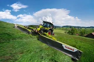 Traktor se širokým žacím strojem CLAAS DISCO 1010 seče louku.