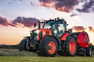 Oranžový traktor Kubota s lisem Kverneland na louce za soumraku.