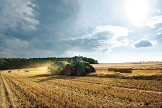 Traktor s lisem Fendt při sklizni slámy na poli.