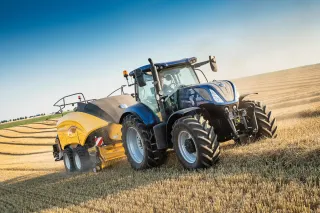 Modrý traktor s lisem New Holland při lisování slámy.