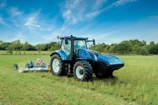 Modrý traktor New Holland Methane Power při sečení louky.