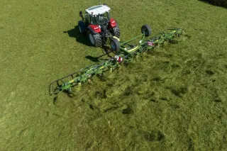 Traktor s rotorovým obracečem Krone Vendro při práci na louce.