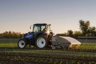 Traktor New Holland s kultivátorem na poli při západu slunce.