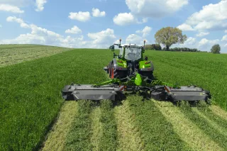 Traktor se širokým žacím strojem Fendt Slicer při sečení louky.