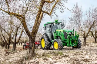 Zelený úzkorozchodný traktor John Deere v ovocném sadu.
