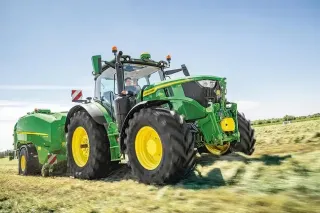 Traktor John Deere s lisem při práci na louce.