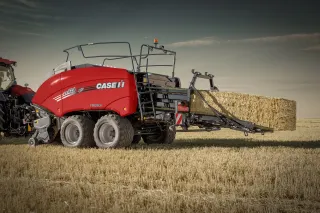 Červený lis Case IH na hranaté balíky při práci na poli.
