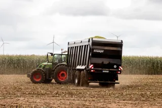 Traktor s černým návěsem Krampe jede po sklizeném poli.