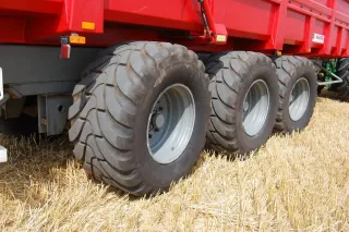 Detail tří velkých zemědělských pneumatik na červeném návěsu.