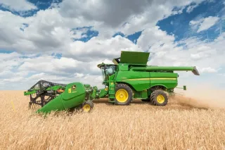Zelená sklízecí mlátička John Deere při sklizni obilí.