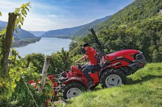 Červený traktor Antonio Carraro ve vinici nad řekou.