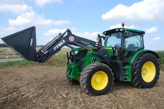 Zelený traktor s čelním nakladačem Stoll na poli.