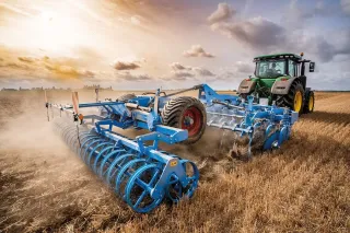 Traktor táhne modré talířové brány Lemken Rubin po strništi.