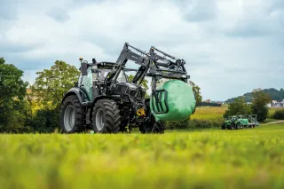 Traktor Deutz-Fahr s kulatým balíkem v předním nakladači.